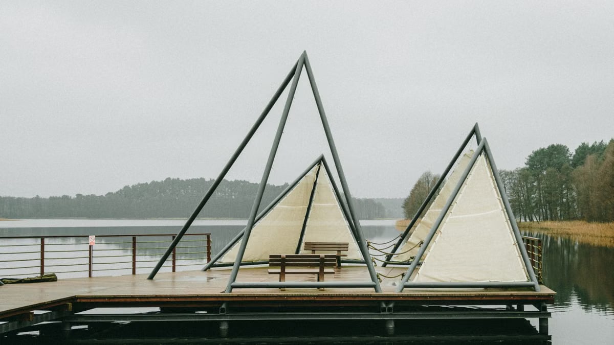 Unique triangular tents sit on a wooden pier overlooking a serene lake in Poland. Perfect for outdoor exploration.